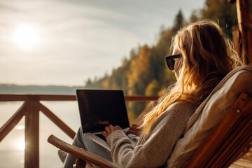 Woman Working on Laptop from Lakeside Cabin Deck at Sunset, Remote Work Retreat.