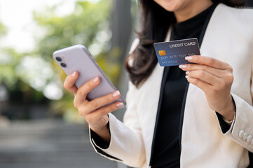 Close up of female office worker businesswoman holding phone and credit card while standing outside