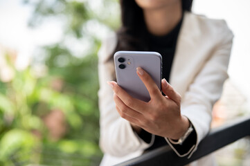 Close up of a female office worker or businesswoman holding phone while standing leaning on railing.