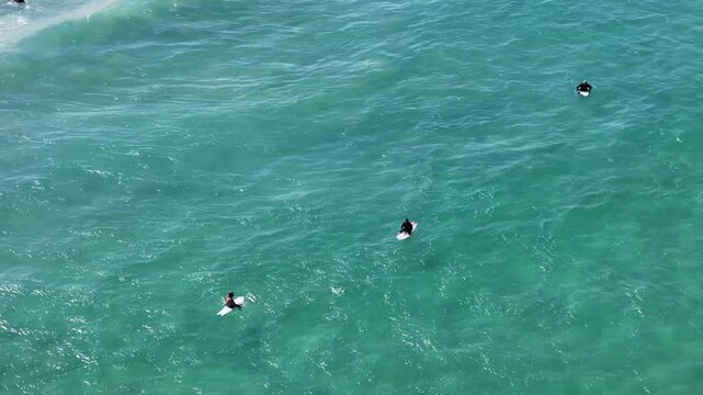 UHD Drone Video - Aerial View of Surfers catching the waves at Wanda Beach in Cronulla on a sunny day with crystal clear water in Sydney, Australia.