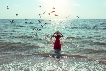 Seascape on a sunny day with seagulls flying over the beach. Young happy woman in a red dress and...