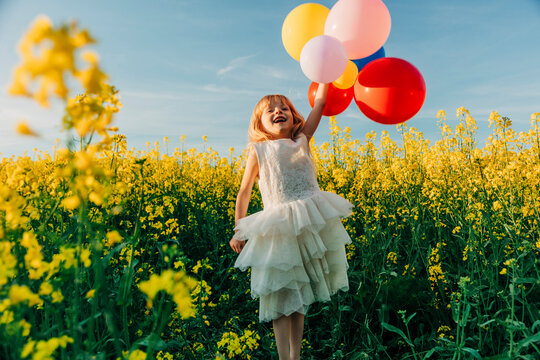 Girl in a white dress holding colorful balloons in a rapeseed field