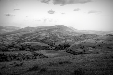 Rolling hills stretch to the horizon under a cloudy sky, capturing the vastness of the landscape with a monochromatic tone.