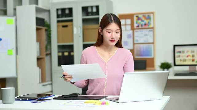 Young female graphic designer using digital tablet and laptop in modern office. Creative workspace, color palettes, and UI UX design in progress.