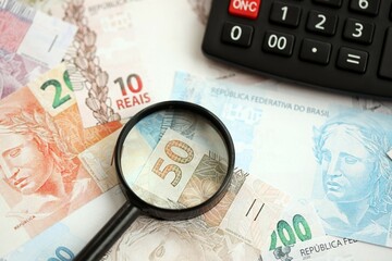 Brazilian reais banknotes and calculator with magnifying glass. Brazil real money, calc with loupe