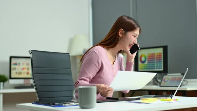Young female graphic designer using digital tablet and laptop in modern office. Creative workspace, color palettes, and UI UX design