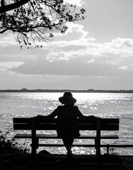 Back view of a woman sitting on a bench, looking out at the sea.