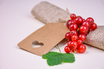 Blank kraft paper label with cut out heart and red currant berries on natural background