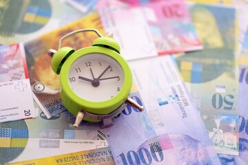 Swiss franc banknotes and alarm clock. The current francs money bills and clock lies on table