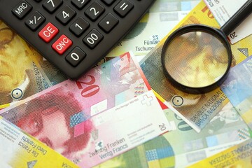 Swiss franc banknotes and calculator with magnifying glass. The current francs money bills and calc