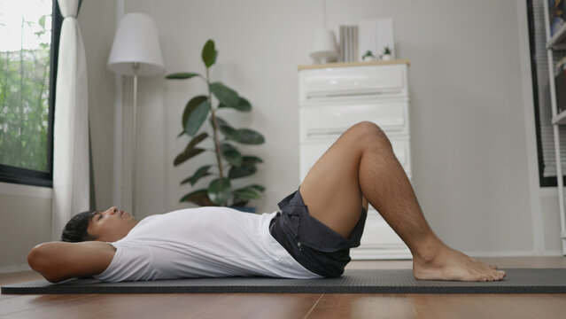 Asian man is performing sit-ups at home. - Powered by Adobe