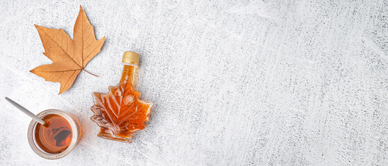 Bottle and glass of tasty maple syrup on grey background