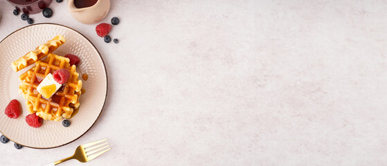 Plate of tasty waffles with berries and maple syrup on white background