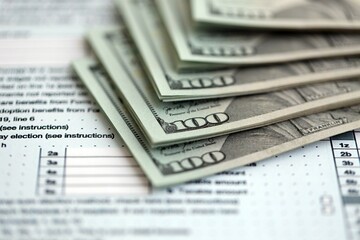 Big amount of United States hundred dollar bills in bunch on table with tax return form