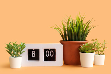Artificial plants with clock on orange background