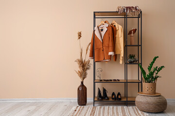 Shelving unit with clothes and shoes near beige wall in hall