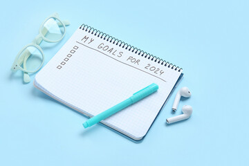 Notebook with empty to do list, eyeglasses and earphones on blue background. New year goals