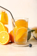 Glass and bottles of infused water with orange slices on white table