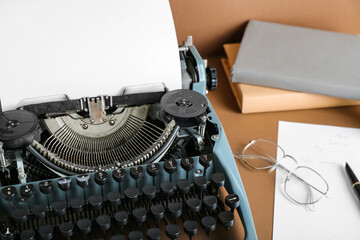 Vintage typewriter with books, eyeglasses and pen on brown background