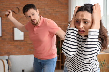 Scared young woman with her angry husband at home. Domestic violence concept