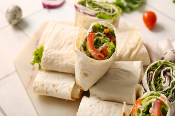 Board of tasty lavash rolls with vegetables on white tile background