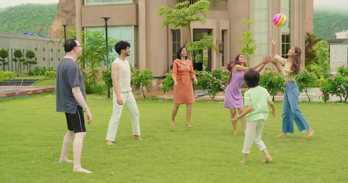 Indian happy family young man woman group play ball game throwing in air have fun joy enjoy outdoor park garden Playful cute teen girl son child kid boy with adult mom lady dad spend day time outside