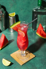 Glass of tasty watermelon cocktail with shakers and lime on grunge green background