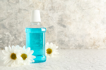 Bottle of mouthwash and chamomile flowers on light table