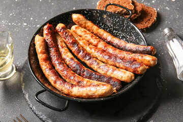 Frying pan of tasty grilled sausages on black background