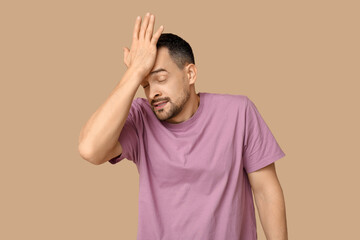 Handsome ashamed young man covering face with hand on brown background