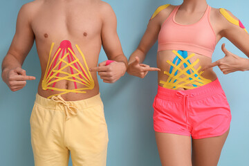 Young couple pointing at physio tape on their bellies blue background