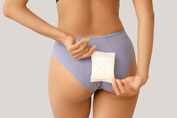 Young woman in menstrual panties with pad on light background, back view