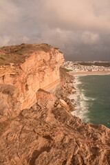 Obraz premium Dramatic sea cliffs bathed in golden light, overlooking São Lourenço Beach and the town of Ericeira, Portugal—famous for its surfing and rugged Atlantic coastline.