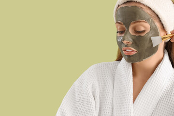Young woman with applied facial mask and brush on green background, closeup