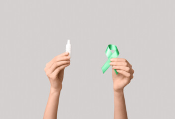 Female hands with green ribbon and eye drops on grey background. Glaucoma awareness concept