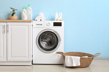 Modern washing machine with basket and cabinet near blue wall. Interior of home laundry room