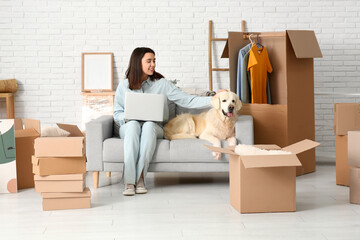 Young happy woman and cute Labrador dog with moving boxes sitting on sofa at home