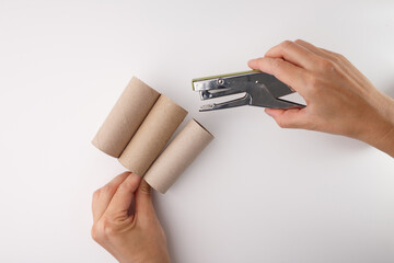 hands-on DIY moment in progress, hand is holding three empty cardboard toilet paper rolls, stapler...