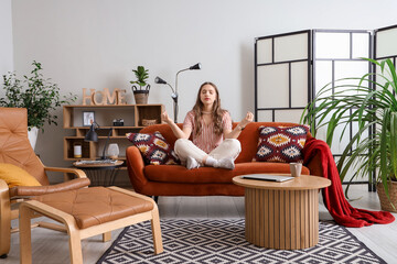 Young woman meditating on red sofa at home