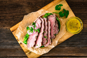 Takeaway sandwich with slices of grilled beef steak on wooden table	