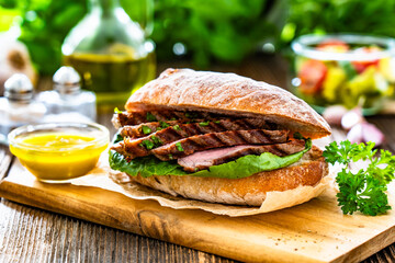 Takeaway sandwich with slices of grilled beef steak on wooden table	