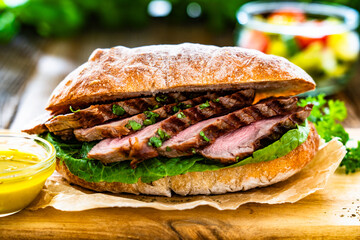 Takeaway sandwich with slices of grilled beef steak on wooden table	