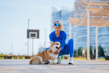 A vibrant individual in all-blue athletic wear, crouching down with a smiling corgi, set against an...