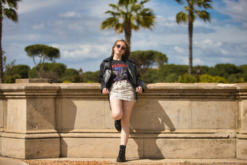 pretty young blonde woman with sunglasses, black leather jacket, boots and short skirt leaning...