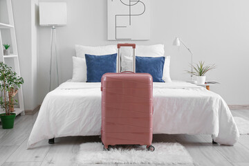 Interior of light hotel room with suitcase near bed