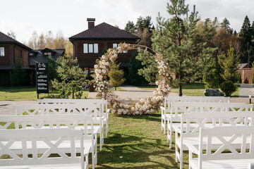 Rustic outdoor wedding setup with circular floral arch and white seating in garden