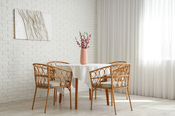 Vase with blooming Sakura branches on table near armchairs in stylish dining room