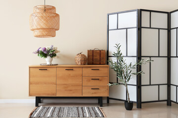 Vase with lilacs on wooden chest of drawers and lamp in stylish room