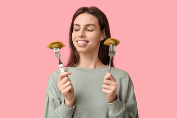 Beautiful young woman holding forks with tasty ravioli on pink background