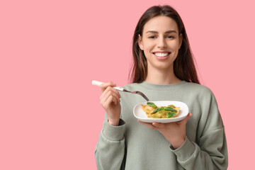 Beautiful young woman eating tasty ravioli on pink background